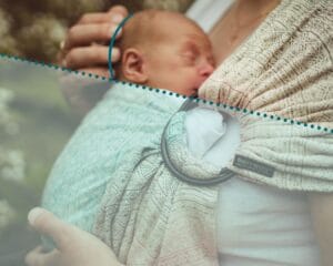 This photo illustrates an important principal of babywearing safety for newborns. The horizontal panel of the carrier is below baby's ear, which means it is also below the base of the baby's skull, leaving the airway neutral and nose open to fresh air.