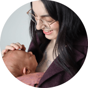 A mother looks at her baby's face, while baby is in a carrier, demonstrating visible and kissable babywearing safety by ensuring she can see the entire face. 